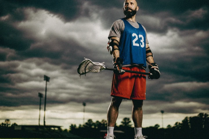 Male lacrosse player holding a lacrosse stick beneath dramatic storm clouds