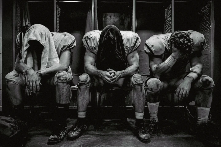 Three exhausted American football players sitting in a locker room after a game
