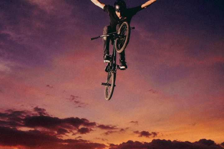 BMX rider performing a no-hander aerial trick against a colourful sunset sky