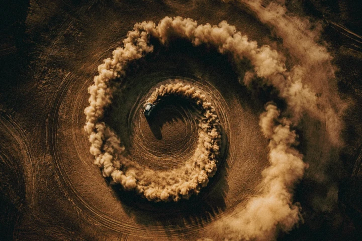 Aerial view of an off-road vehicle creating circular tyre tracks and a large spiral of desert dust