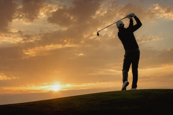 A golfer completes a powerful full swing against a dramatic golden sunset, photographed for golf clubs, tournaments and sports campaigns across Dubai, Abu Dhabi and the UAE.