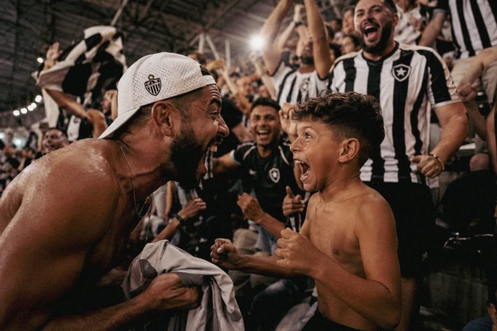 Adult football supporter and young boy shouting with excitement among celebrating fans