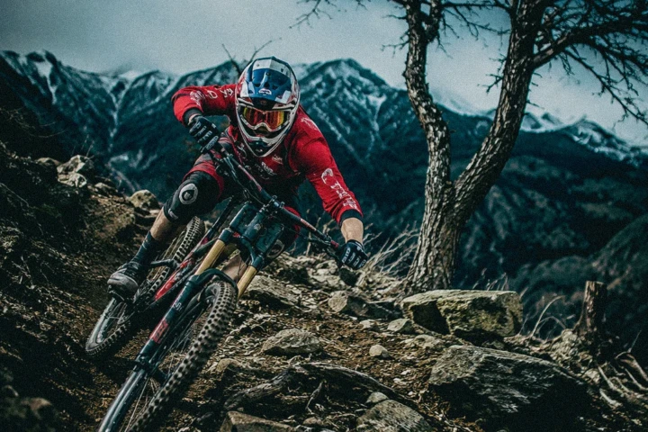 Downhill mountain biker in red riding aggressively through a rocky mountain trail