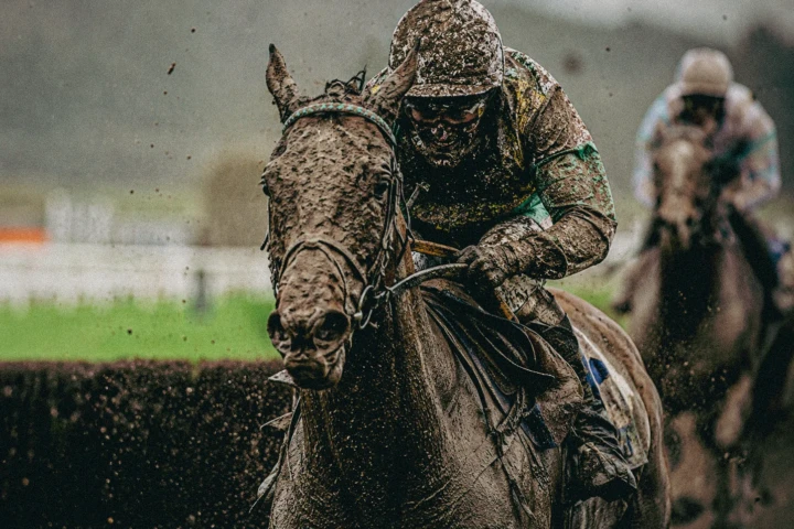 Mud-covered jockey riding a racehorse at speed during a wet steeplechase race