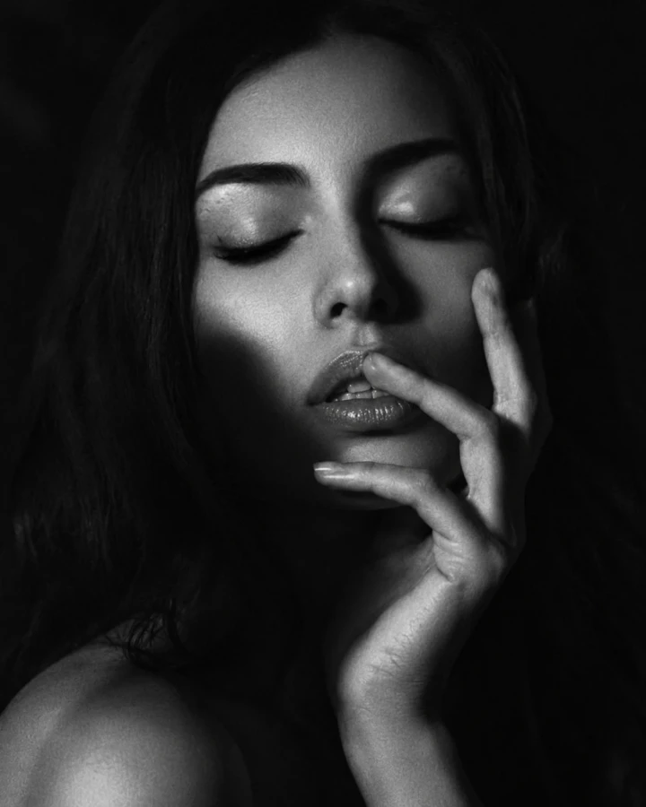 Black and white beauty close-up of an adult woman with closed eyes and one hand gently framing her lips and face.