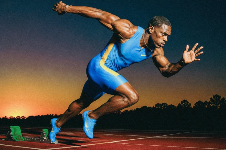 Male sprinter accelerating from starting blocks on an outdoor running track at sunset