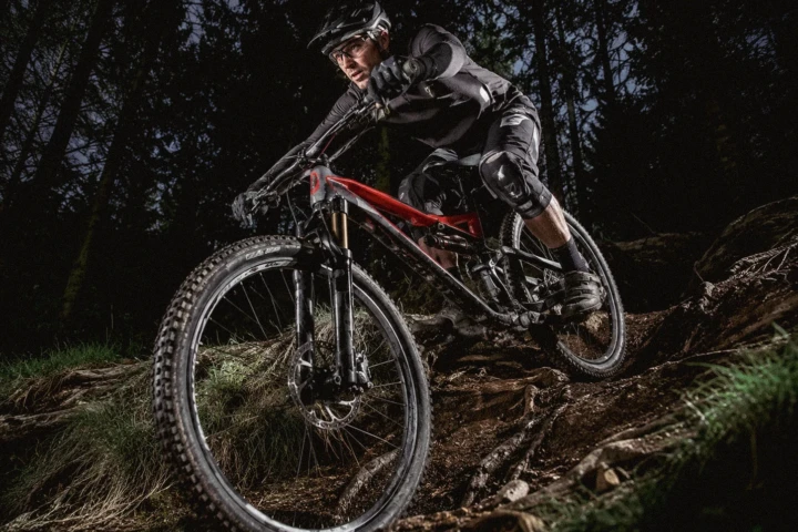 Mountain biker riding a red full-suspension bicycle down a steep forest trail