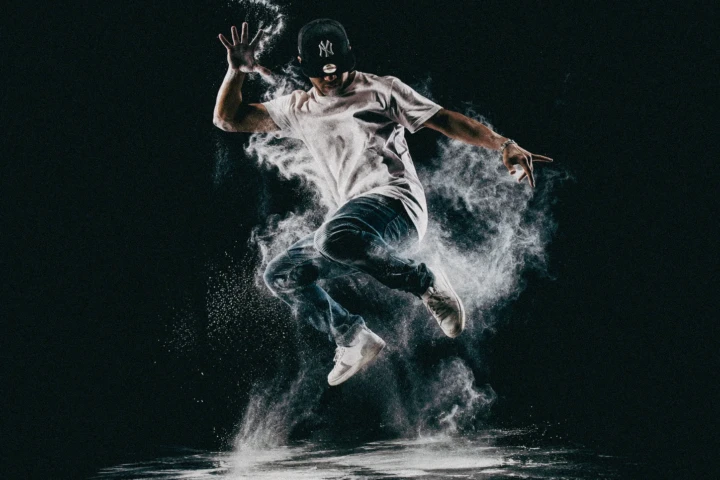 Urban dancer jumping through white powder against a dark studio background
