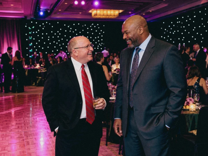 Two business executives sharing a candid conversation during a formal corporate evening event.