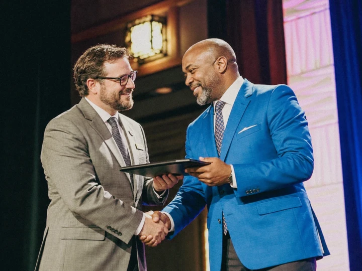 Two executives shaking hands during a formal award presentation on stage at a corporate event.