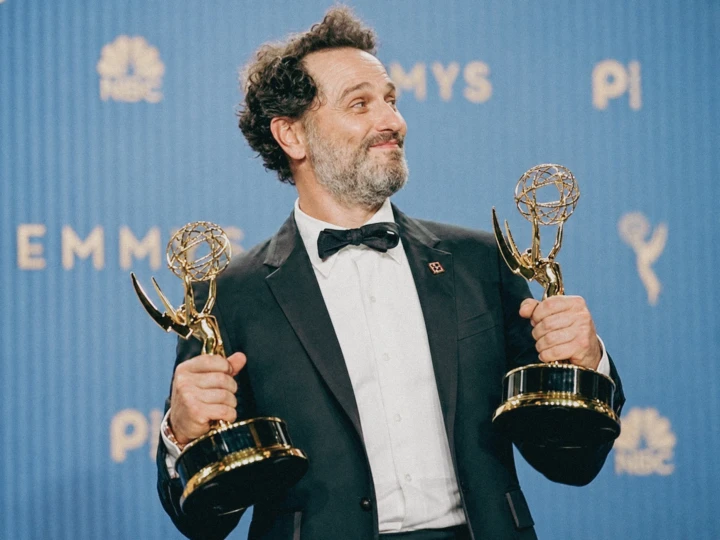Award winner holding two trophies in front of a branded media backdrop during a formal professional event.