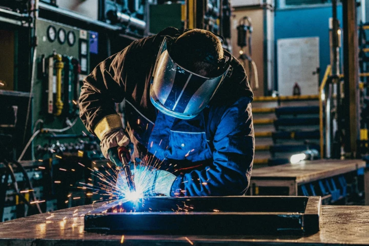 Welder fabricating a steel frame with bright welding sparks inside an industrial metal workshop in Dubai, UAE.