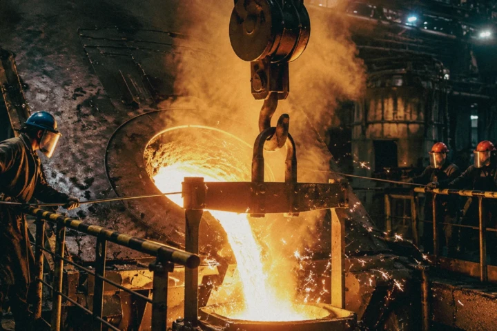 Steel foundry workers monitoring molten metal pouring from an industrial furnace during heavy manufacturing photography in Dubai, UAE.