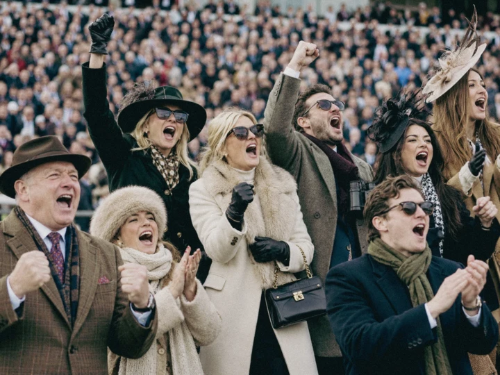 Excited race day spectators cheering from the stands during a high-energy horse racing event.