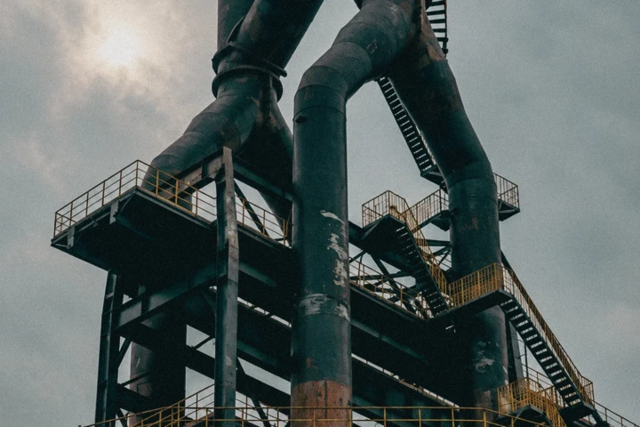 Low-angle view of large industrial processing towers, ducts, steel platforms and access stairs inside a heavy industry facility in the UAE.