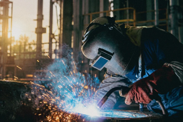 Industrial welder performing metal fabrication with bright welding sparks inside a production facility in Dubai, UAE.