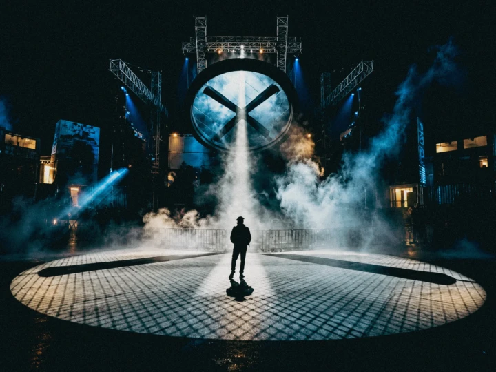 Dramatic live event stage with a silhouetted guest, theatrical lighting, smoke effects and large-scale production rigging.