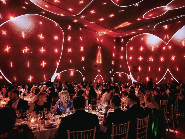 Large formal gala dinner with guests seated beneath immersive red projection lighting and premium event production.