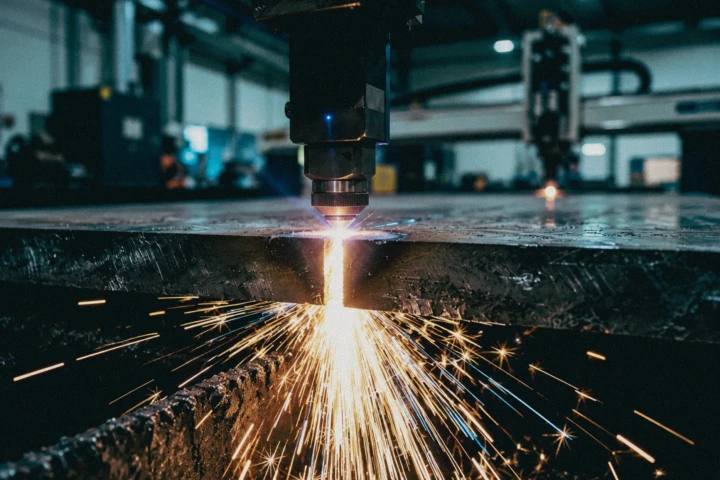 Industrial laser cutting machine processing a thick metal sheet with sparks inside a manufacturing facility in Dubai, UAE.
