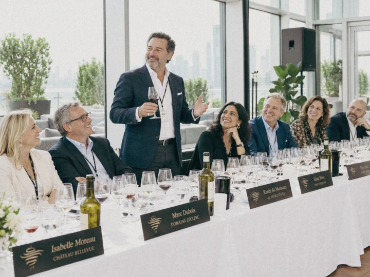 Business guests gathered around a tasting table while a speaker addresses the group during a corporate networking event.