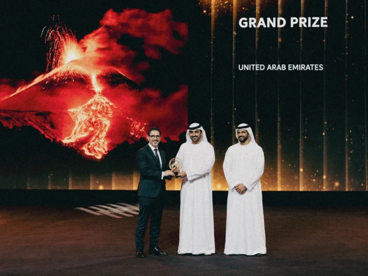 Three guests on stage during a formal UAE Grand Prize award presentation with the trophy displayed in front of a large event screen.