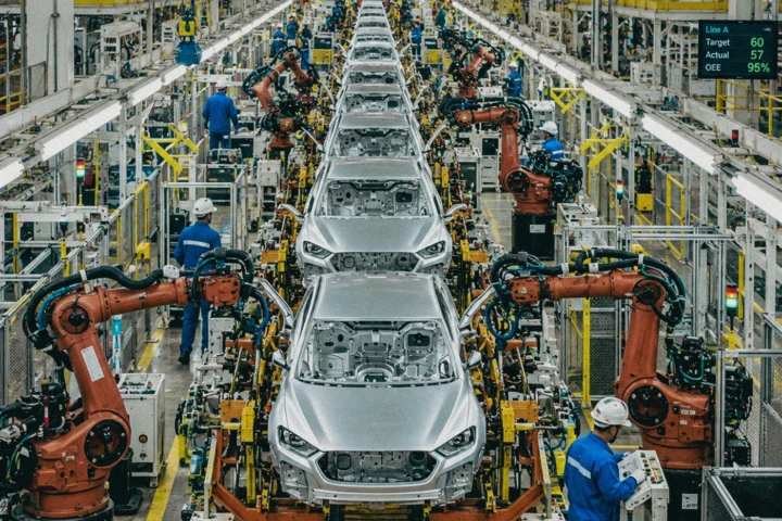 Automated automotive production line with robotic arms, vehicle bodies and factory workers inside a manufacturing facility in Dubai, UAE.