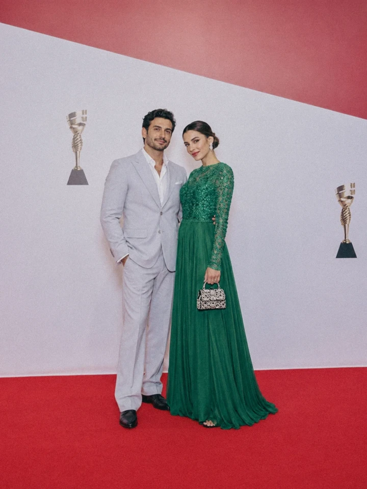 Elegant couple posing on a red carpet in front of an event media wall during a formal VIP event.