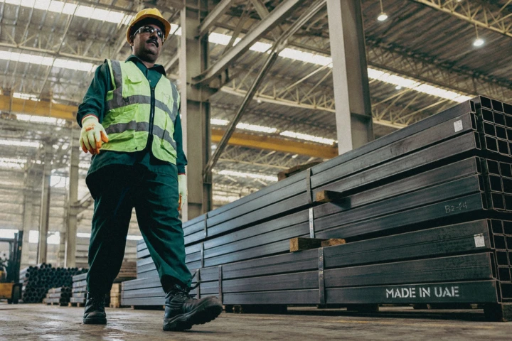 Industrial worker walking beside stacked fabricated steel sections inside a UAE manufacturing facility.