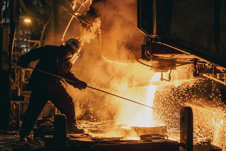 Steelworker handling molten metal during a high-temperature manufacturing process inside a heavy industrial foundry.